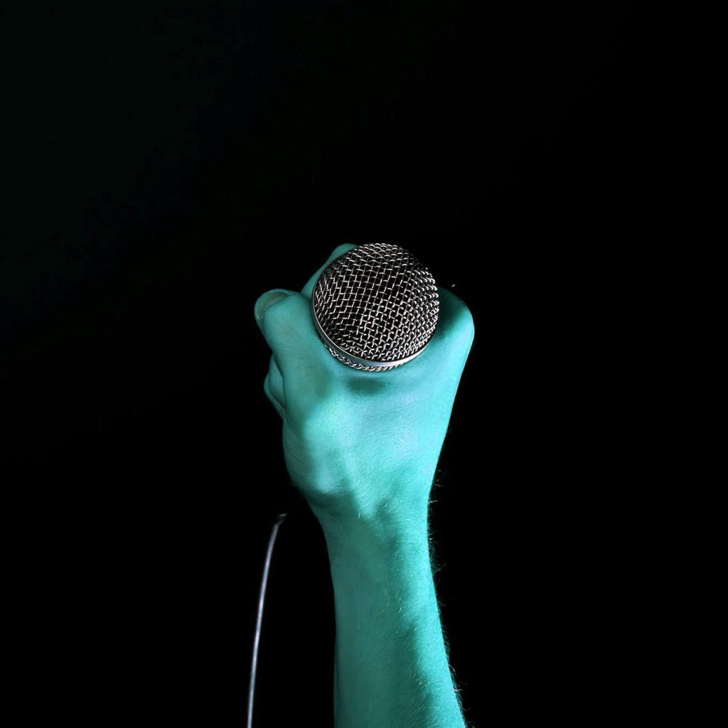 A blue hand holding a microphone against a black background.