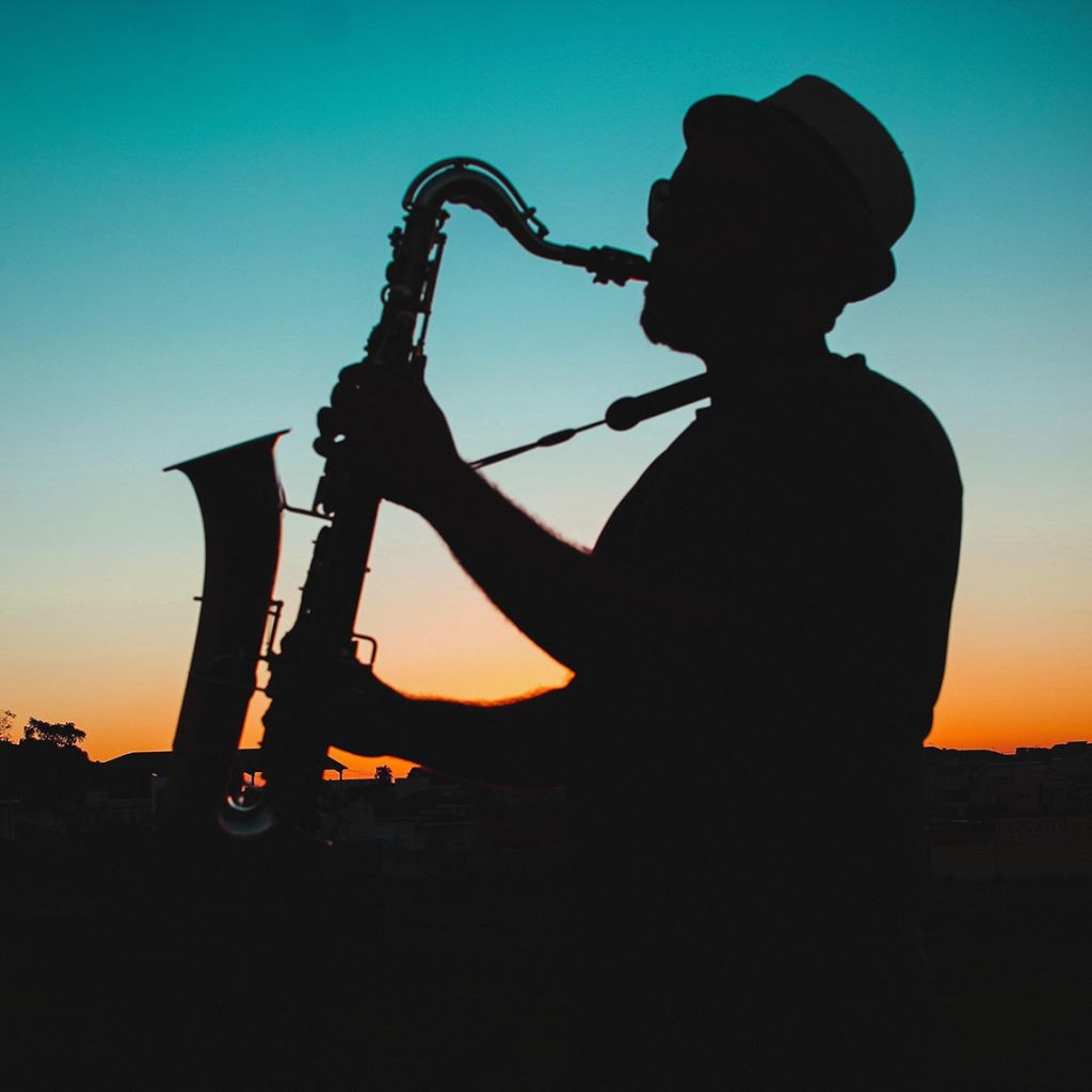 A silhouette of a man playing saxophone in front of a sunset.